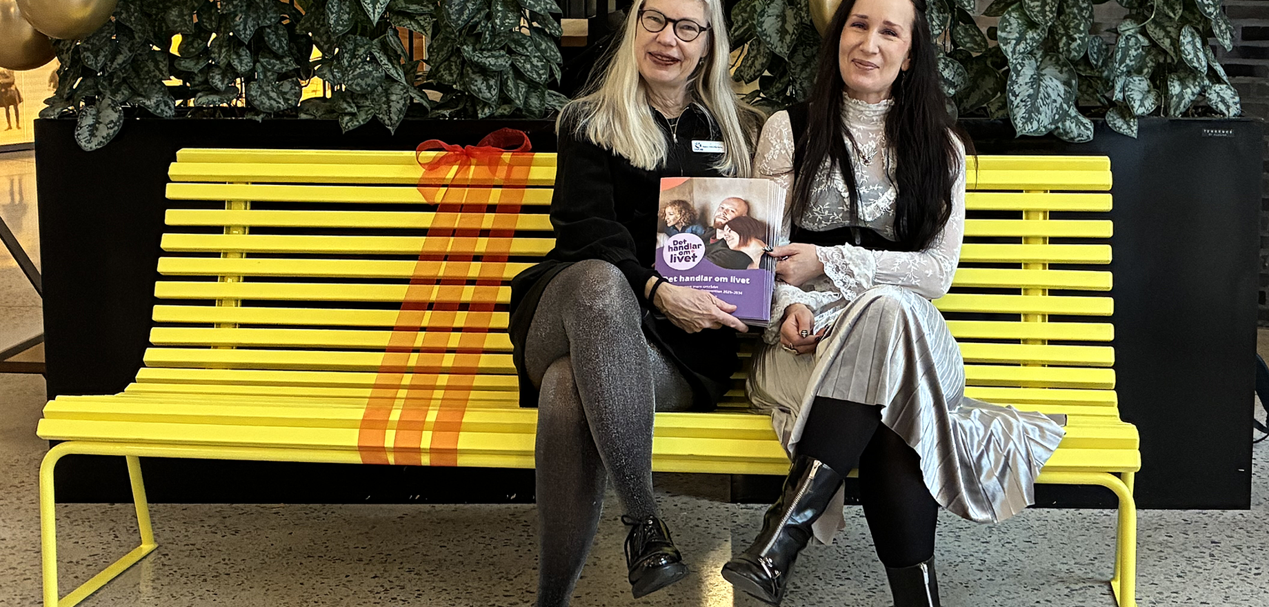 Två kvinnor sitter på en gul bänk.