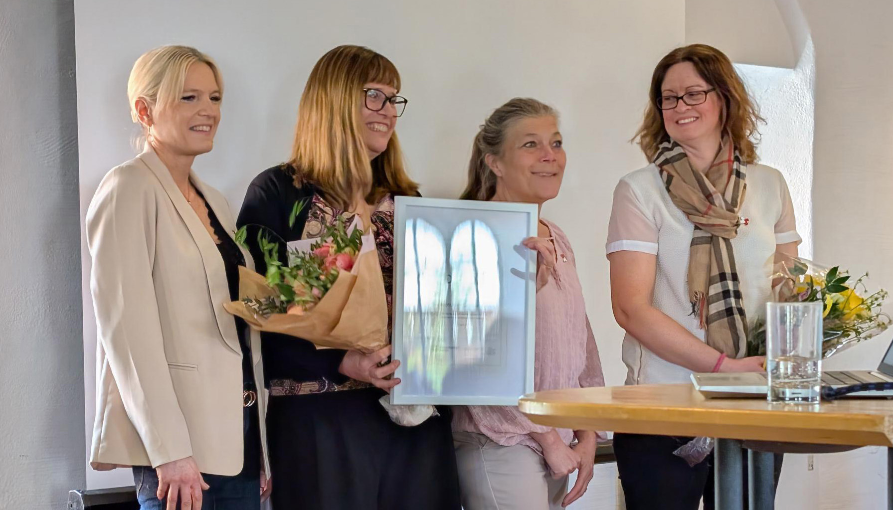 Fyra kvinnor på ett podie med blommor och diplom