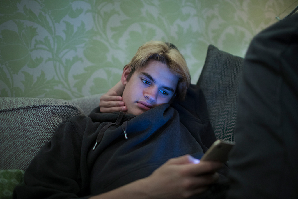 En ung kille sitter i soffa med en mobil i handen. Foto: Caia Image/Johnér Bildbyrå