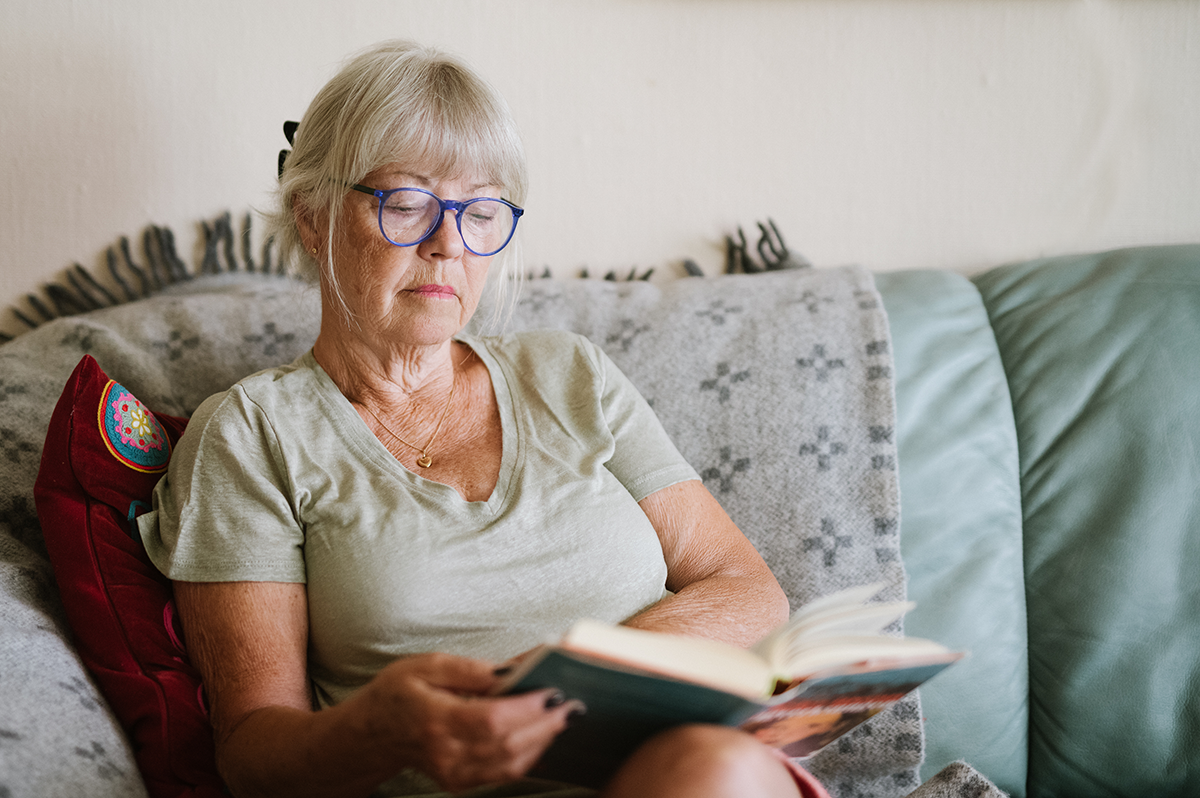 Äldre kvinna sitter i en soffa och läser en bok