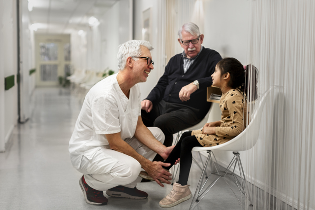 En ung flicka och en äldre man pratar med en läkare i en sjukhuskorridor