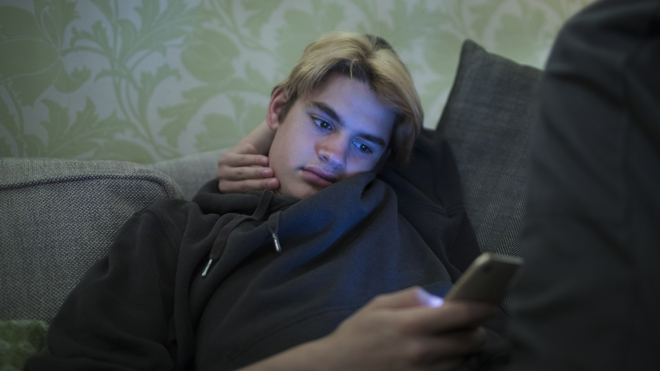En ung kille sitter i soffa med en mobil i handen. Foto: Caia Image/Johnér Bildbyrå