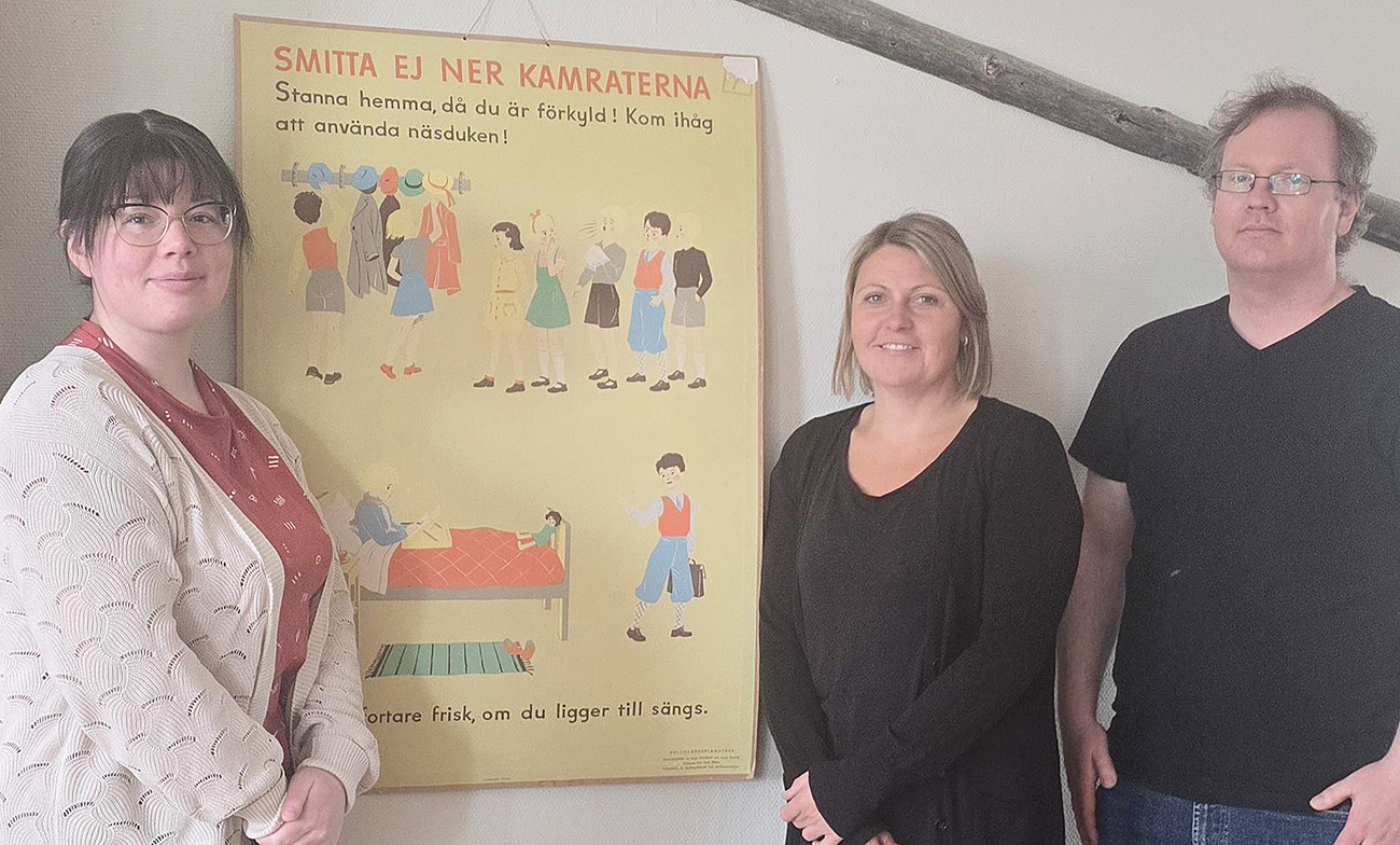 Tre personal står framför en gammal plansch