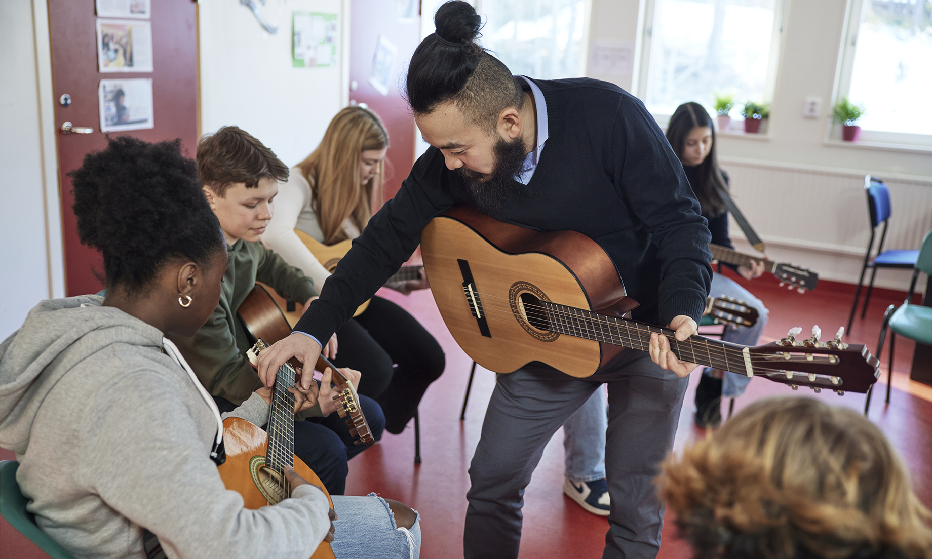 En ledare håller i en gitarr och pratar med barn som också har gitarrer