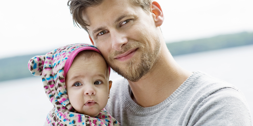 Ljushårig man i 30-årsåldern håller en bebis i famnen.